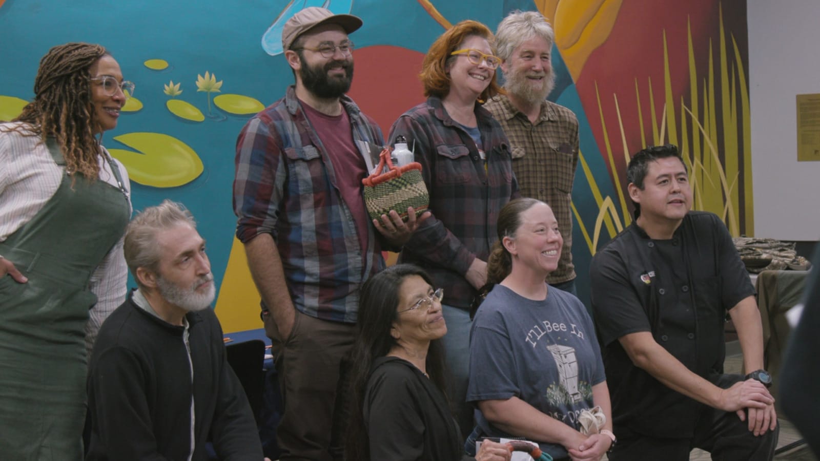 Folks pose for a photo while holding baskets of goodies in front of a colorful mural.