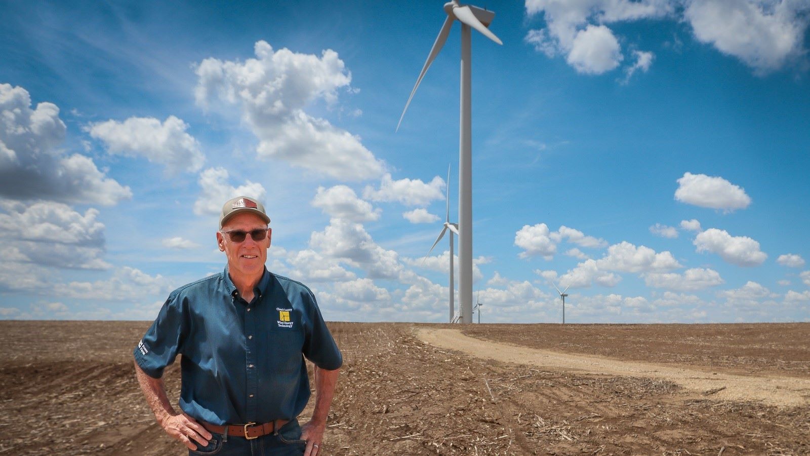 Bruce Graham, former head of the Renewable Energy Department at Cloud County Community College in Concordia, Kansas, stands in front of a wind turbine.