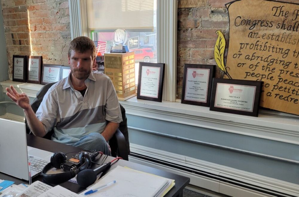 News editor and co-publisher Will Brumleve sits at his desk at the Ford County Chronicle in front of awards and text from the First Amendment. He and co-founder Andrew Rosten launched the newspaper in Paxton, Illinois, in 2020, one of the few new papers in the U.S. in recent years.