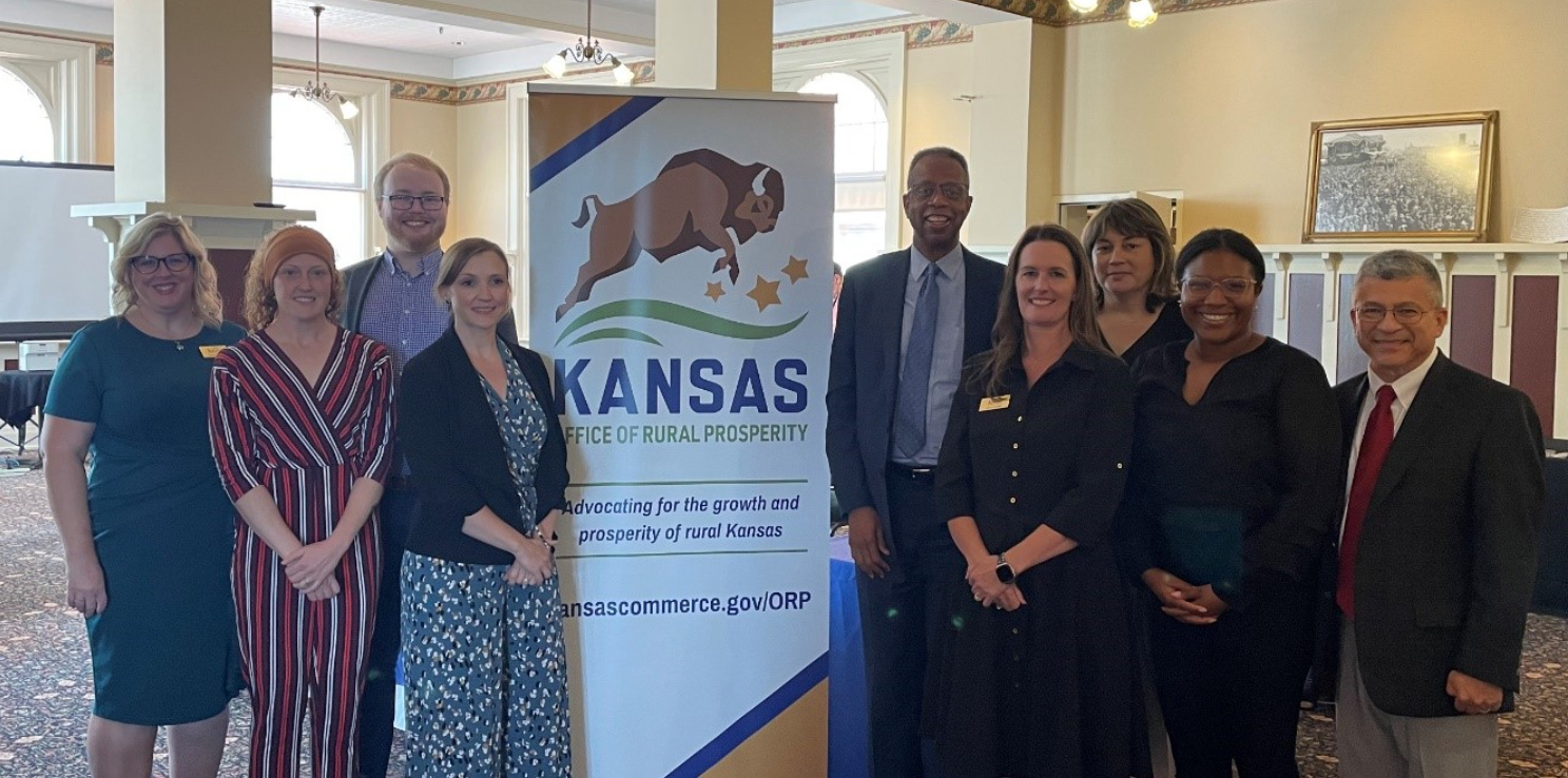A group of people stand next to a sign with a buffalo that reads "Kansas Office of Rural Prosperity"