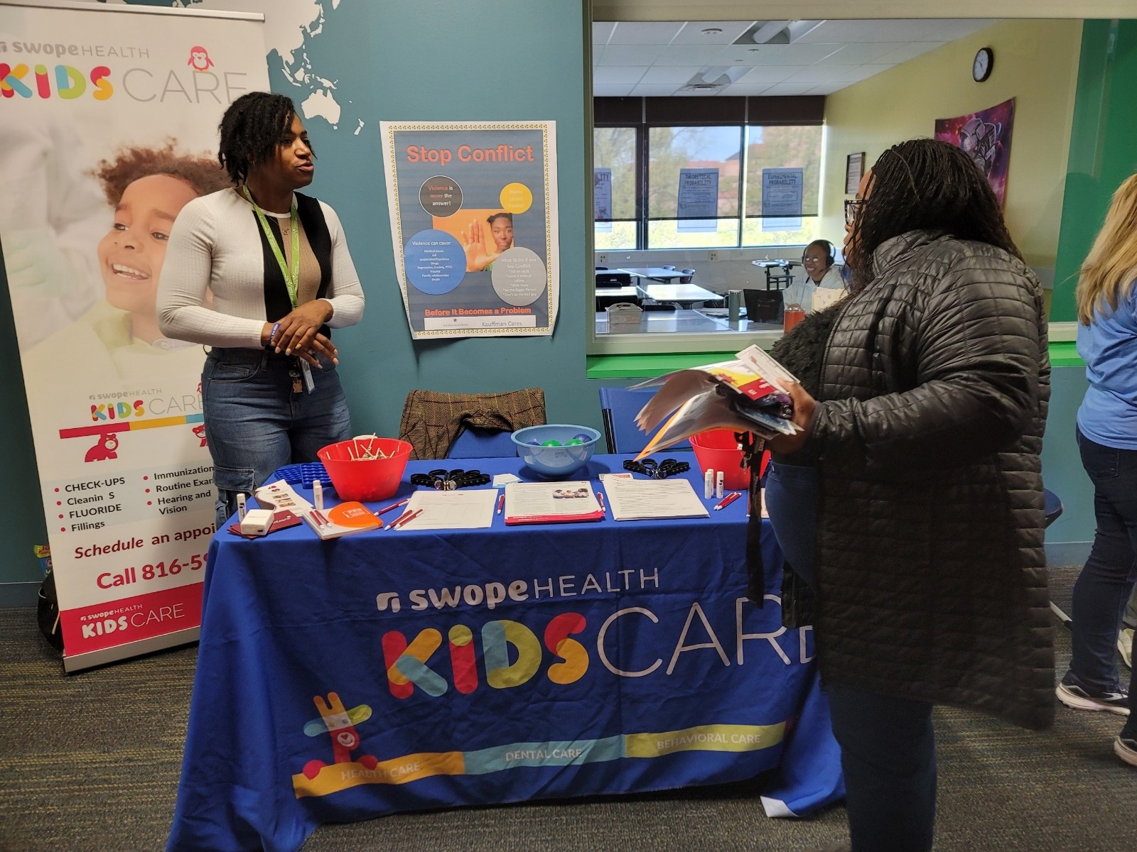 Two people stand by a Kids Care table, covered with a blue cloth for Swope Health