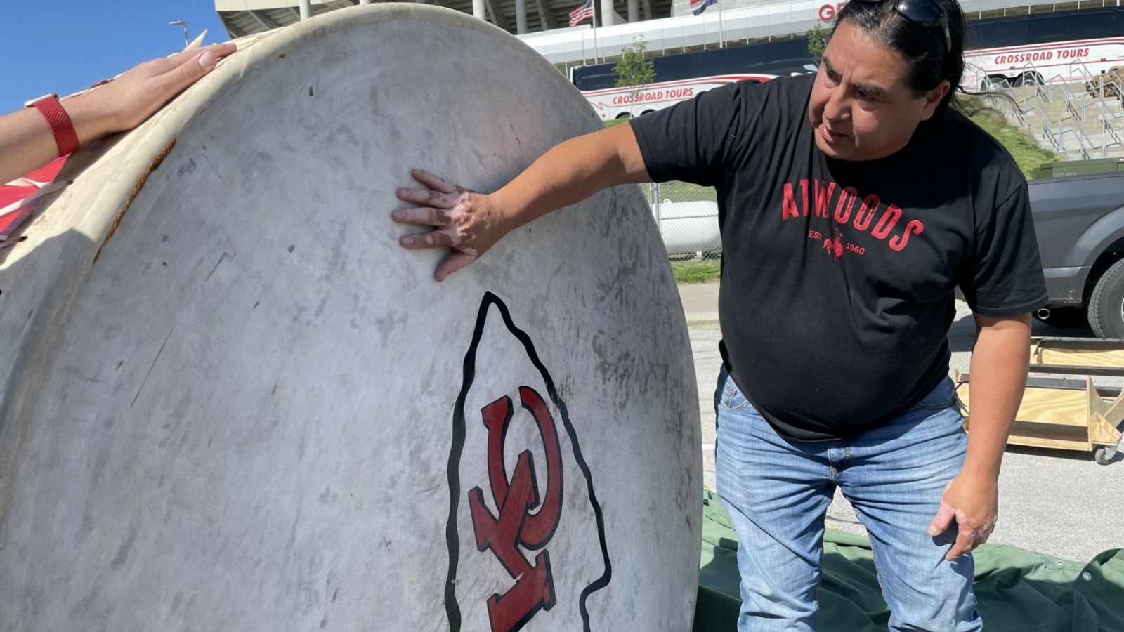 A man in a black t-shirt and jeans standing beside a large drum with a KC Chiefs logo.