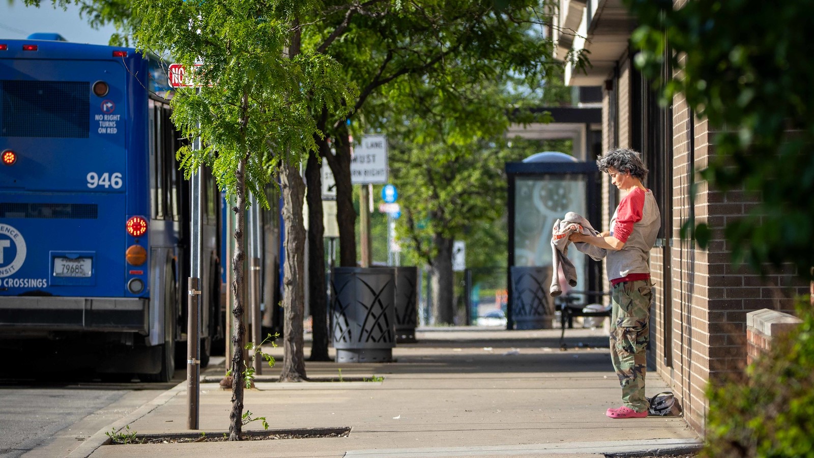 A person stands on the sidewalk near a bus stop just south of the Lawrence Public Library.