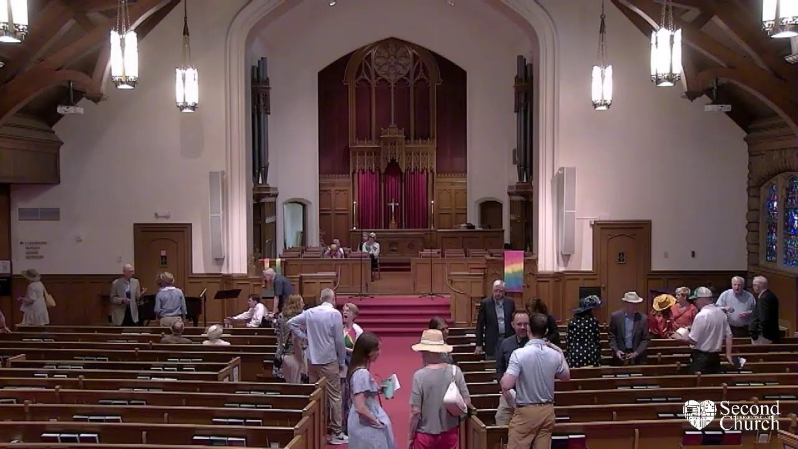 A Sanctuary of a church with people standing in the pews and aisle.