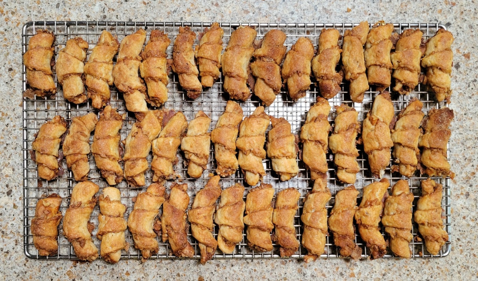A sheet of crescent shaped tan-colored cookies called Rugelach sit on a countertop.