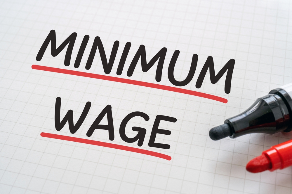 The words Minimum Wage are written in black ink with red underlines on a piece of graph paper with a red and black marker sits next to them on the page.