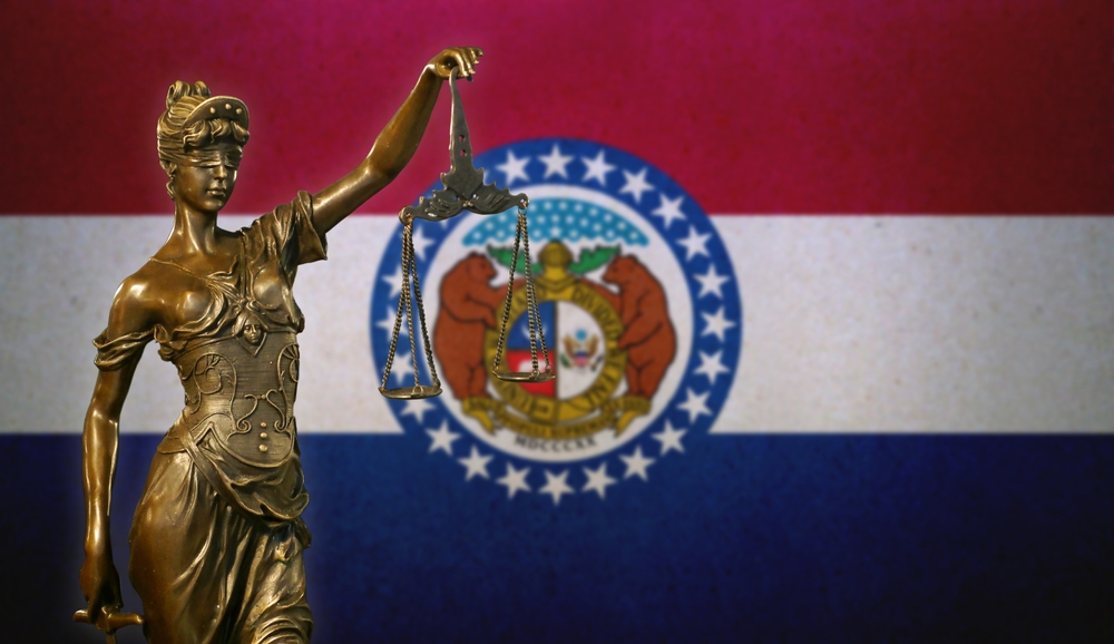 Close-up of a small bronze statuette of Lady Justice before a flag of Missouri.