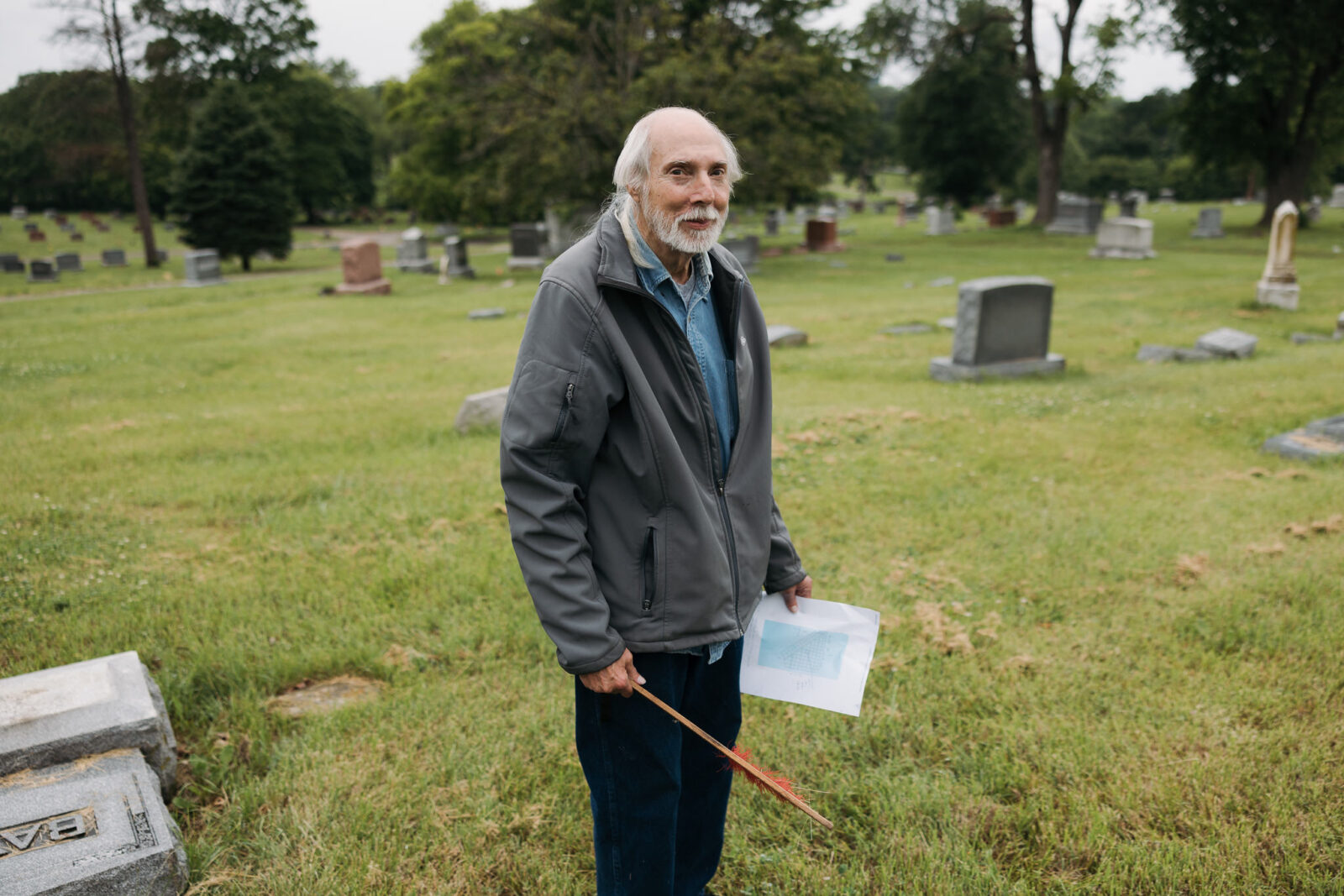 Robert Franke stands for a photo with a map and a brush for clearing gravestones at Forest Hill Cemetery, off Troost in Kansas City, Missouri. Franke gathers users’ search requests at findagrave.com to generate a list of names and info he uses to locate the grave sites. (Chase Castor | Flatland