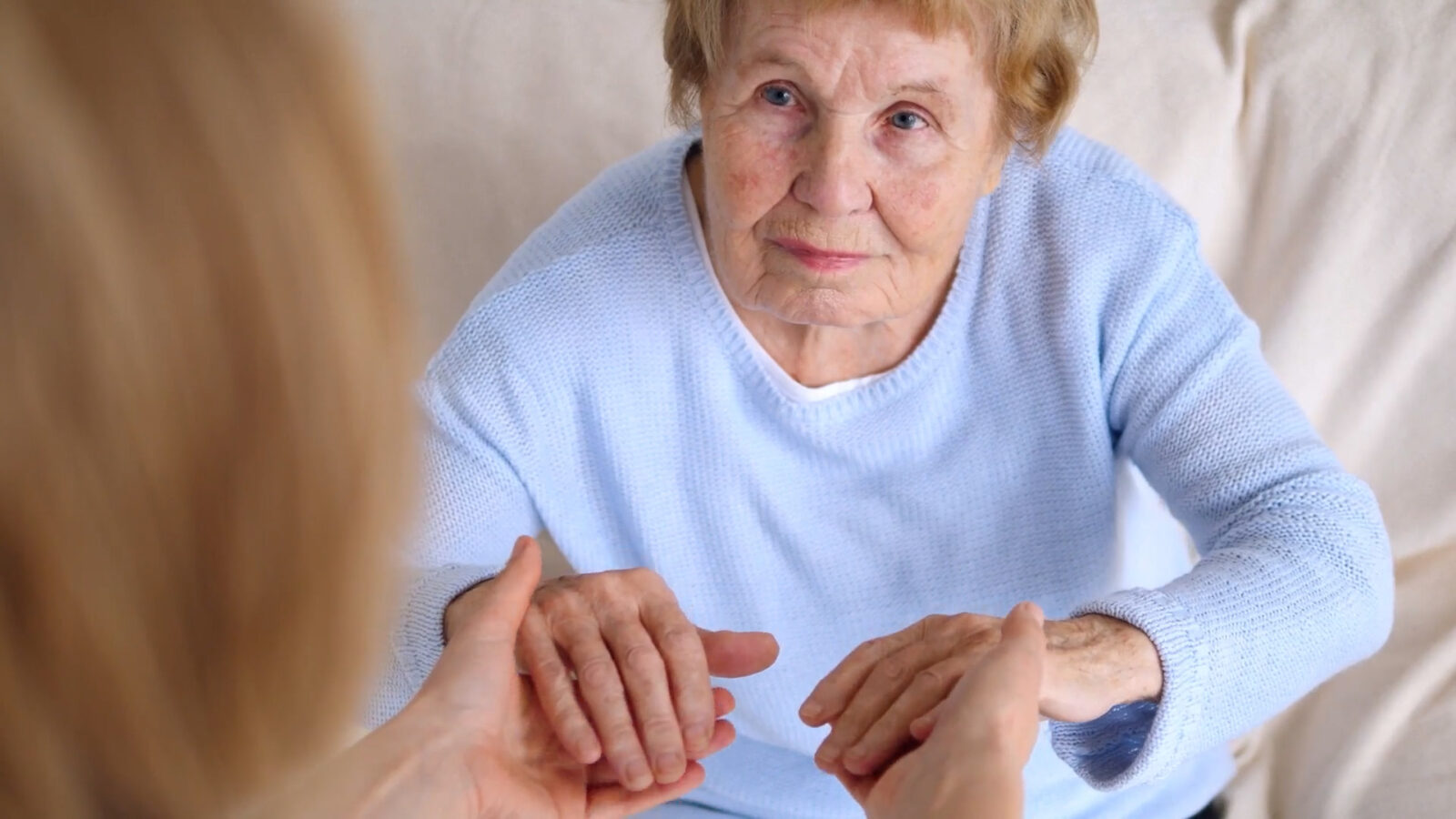 Elderly woman holding hands with unseen caregiver
