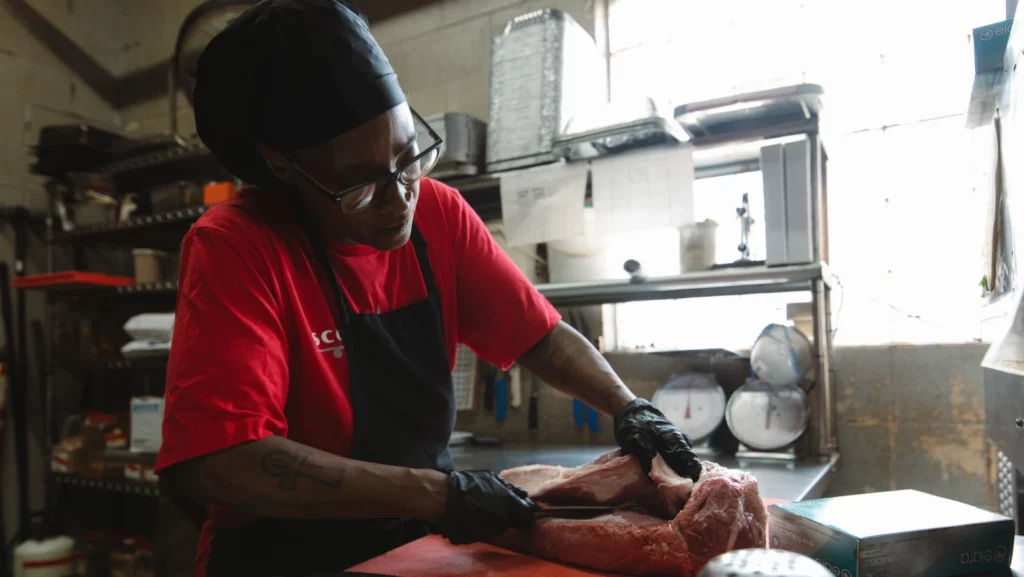 Image Credit: Veronica Scroggins trims brisket at Scott’s Kitchen & Catering at Hangar 29 in Kansas City, North. (Chase Castor | Flatland)
