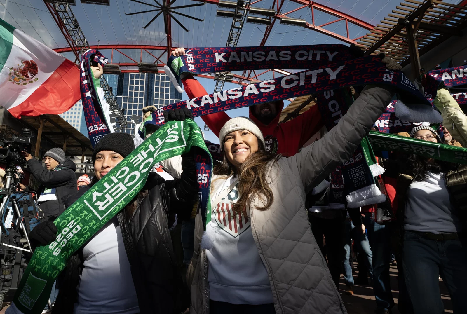 Scarves aloft, Ali Samaniego, at left, and Veronica Brewer celebrate at a regionwide watch party for the final draw. In the countdown to the FIFA World Cup, the event drew a crowd Friday morning to KC Live! in the Power & Light District. (Julie Denesha | KCUR 89.3)