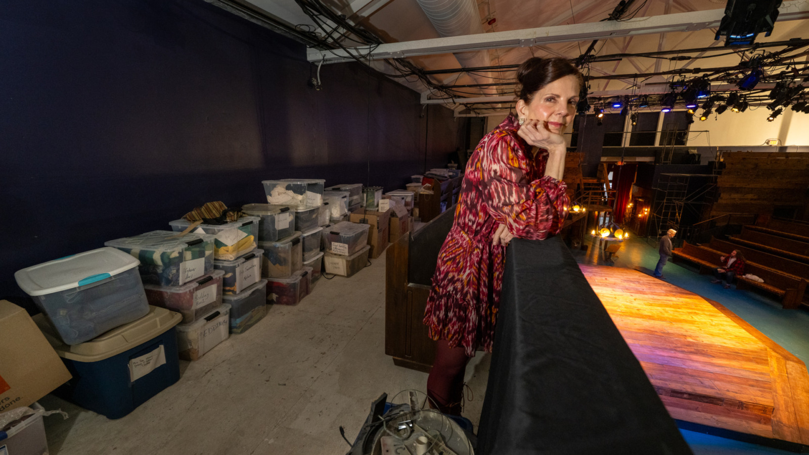 Karen Paisley, artistic director and cofounder of the Metropolitan Ensemble Theatre, stands in a balcony above the stage at the Warwick Theatre. Behind her are storage tubs full of costumes that she and volunteers cleaned after a devastating fire at the site two years ago, on Feb. 6, 2024. (Todd Feeback | Flatland)