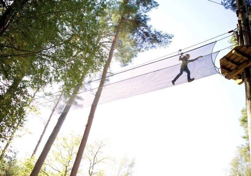 A person climbs across a rope bridge in treetops.