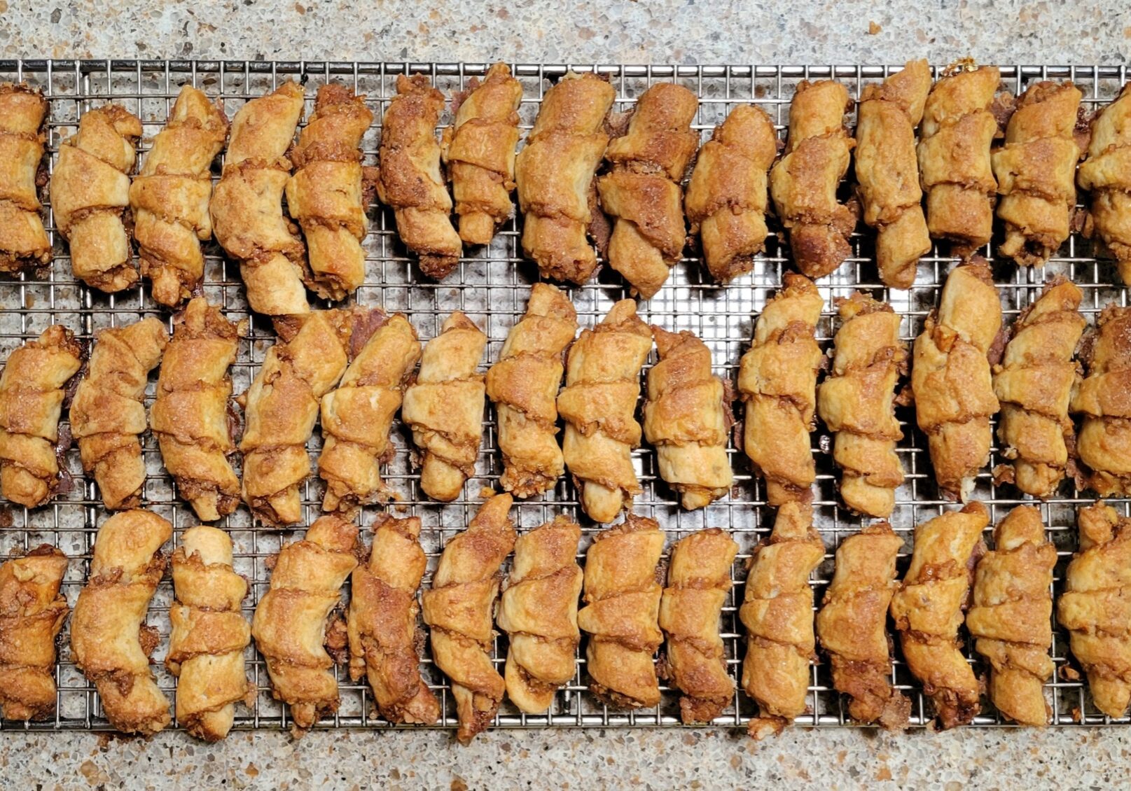A sheet of crescent shaped tan-colored cookies called Rugelach sit on a countertop.