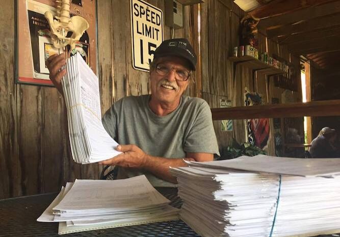 man with hat and glasses holds up papers.