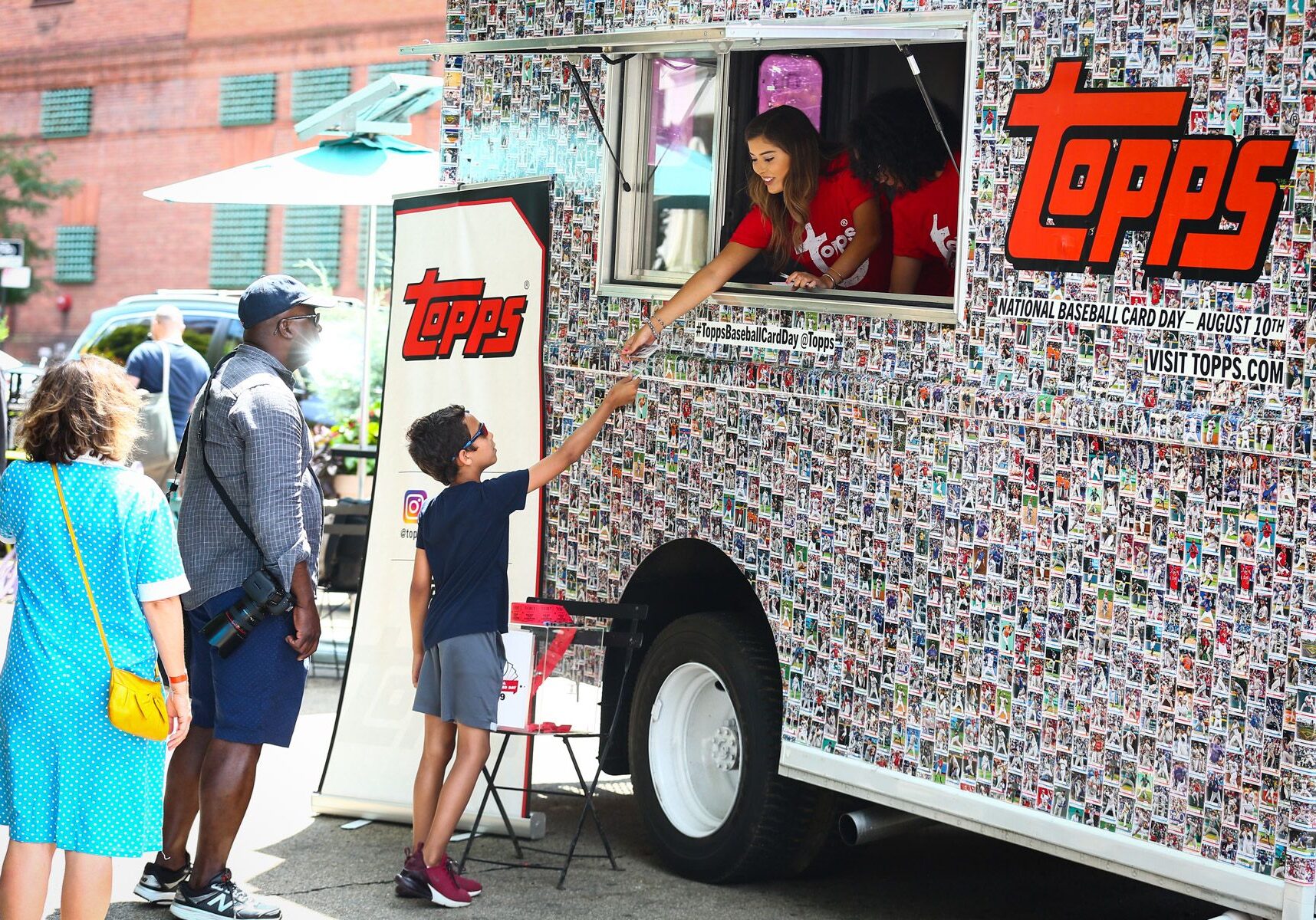 A boy is handed trading cards from a Topps Truck decorated with baseball cards.