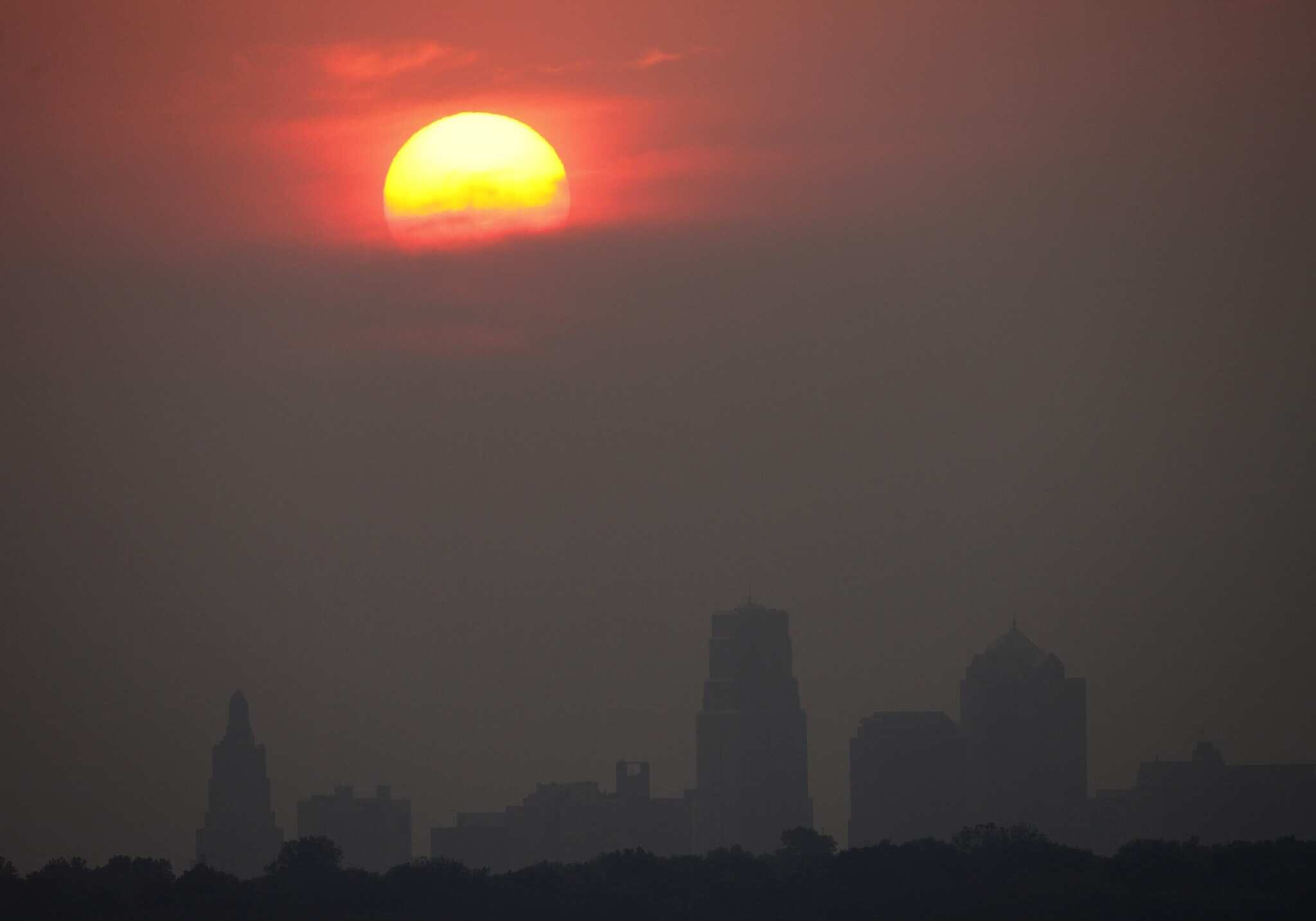 The setting sun is shrouded in hazy clouds as it sets beyond downtown Kansas City, Mo. Monday, June 13, 2011. Smoke from massive wildfires in Arizona has created brilliant sunsets in states as far away as Kansas and Nebraska. (AP Photo/Charlie Riedel)