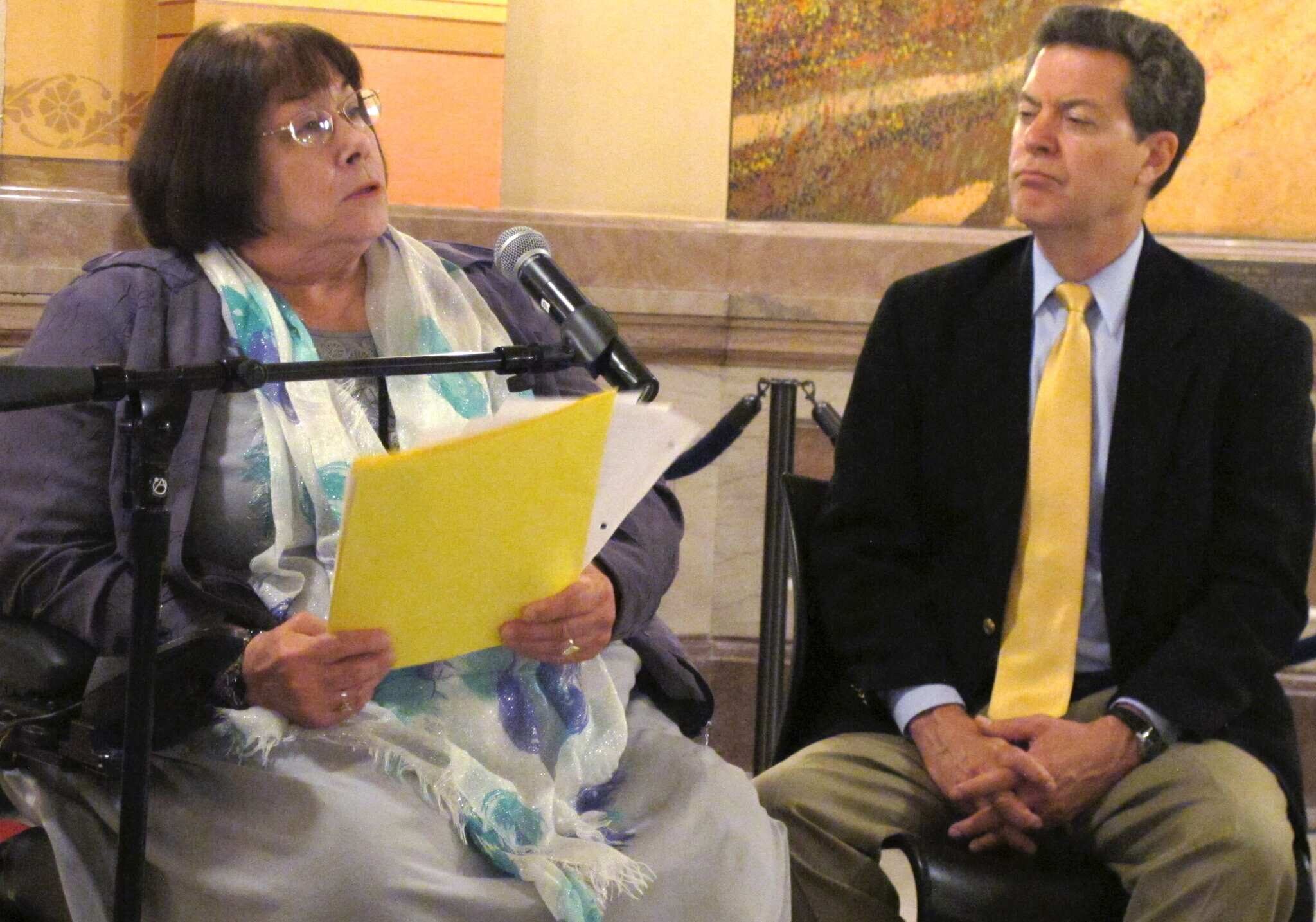 Phyllis Gilmore, left, Kansas secretary for children and families, discusses new mental health initiatives as Gov. Sam Brownback, right, watches, during a news conference, Tuesday, May 27, 2014, at the Statehouse in Topeka, Kan. Brownback's administration announced it is putting $9.5 million in state and federal funds into mental health services. (AP Photo/John Hanna)