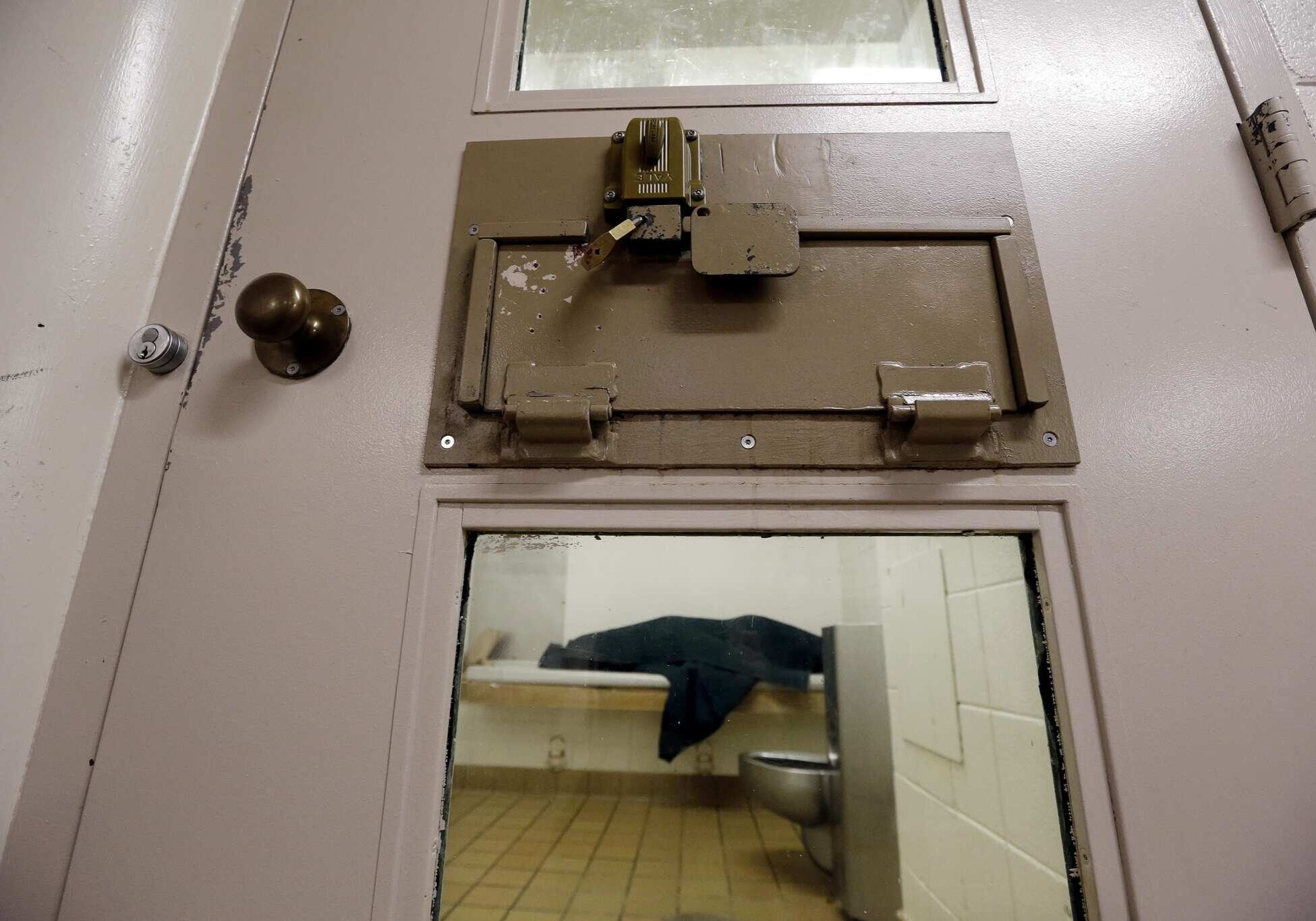FILE - In this photo taken Oct. 15, 2014, an inmate huddles under a heavy blanket on a bunk in the psychiatric unit of the Pierce County Jail in Tacoma, Wash. Washington state, under scrutiny for holding mentally ill people in jails instead of providing timely competency evaluations and treatment, is fighting efforts to have a federal judge rule quickly in favor of the defendants. (AP Photo/Elaine Thompson, file)