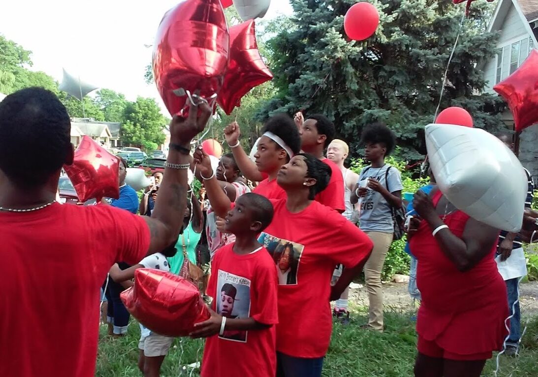 crowd of people in red t-shirts with red balloons at a memorial vigil.
