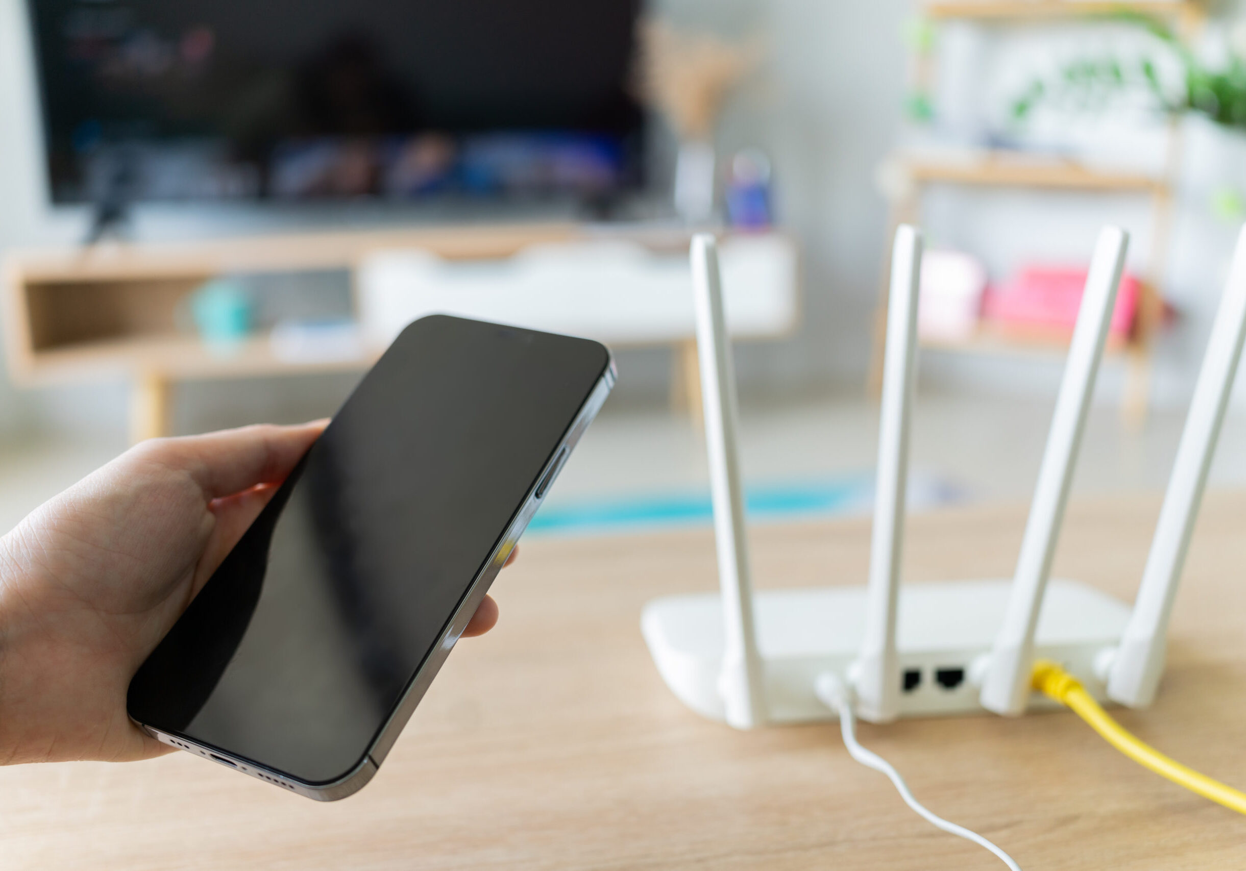 Wi-Fi router sits on a table while someone holds a smartphone.