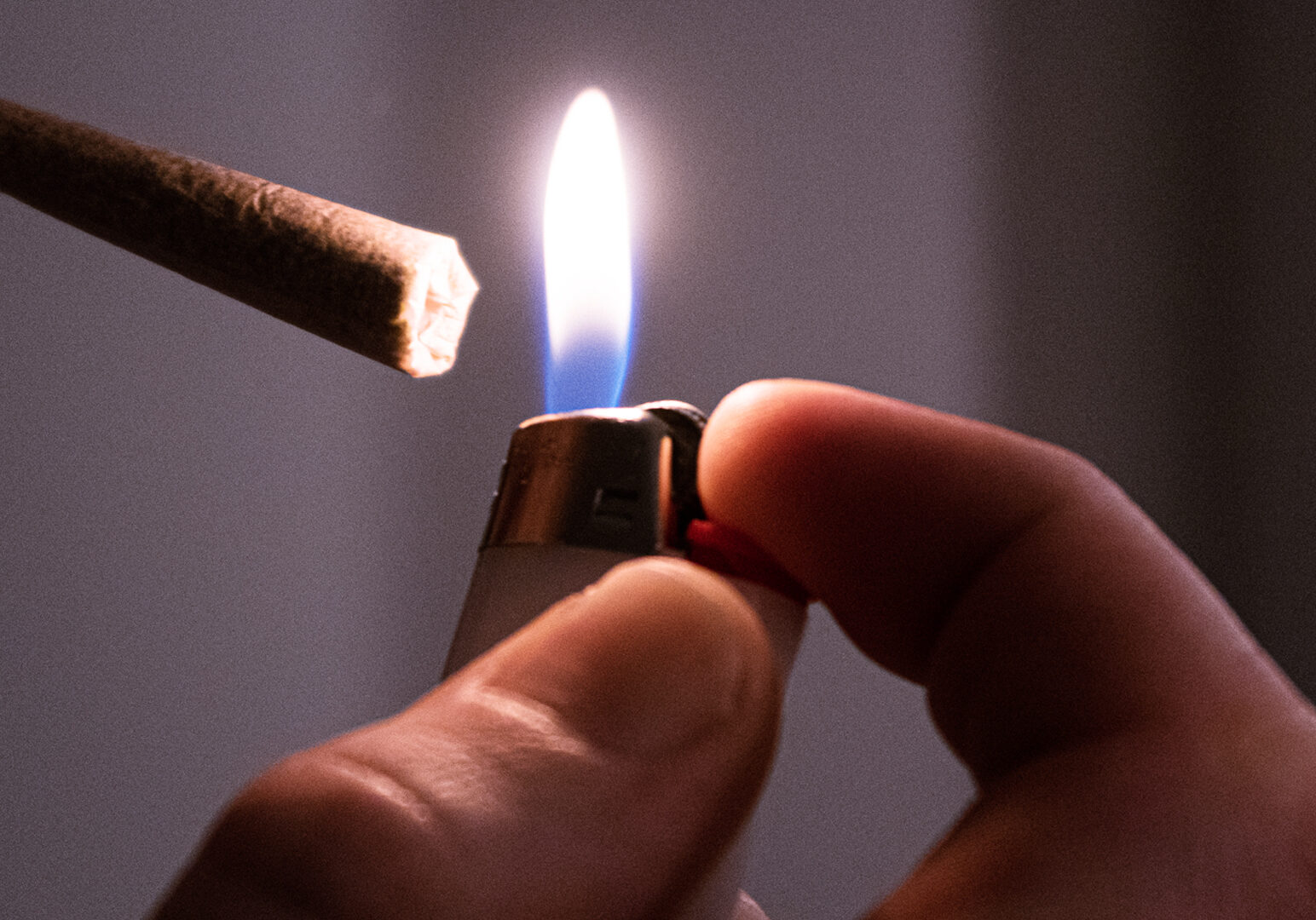Close up of a hand holding a lighter up to the end of a joint.