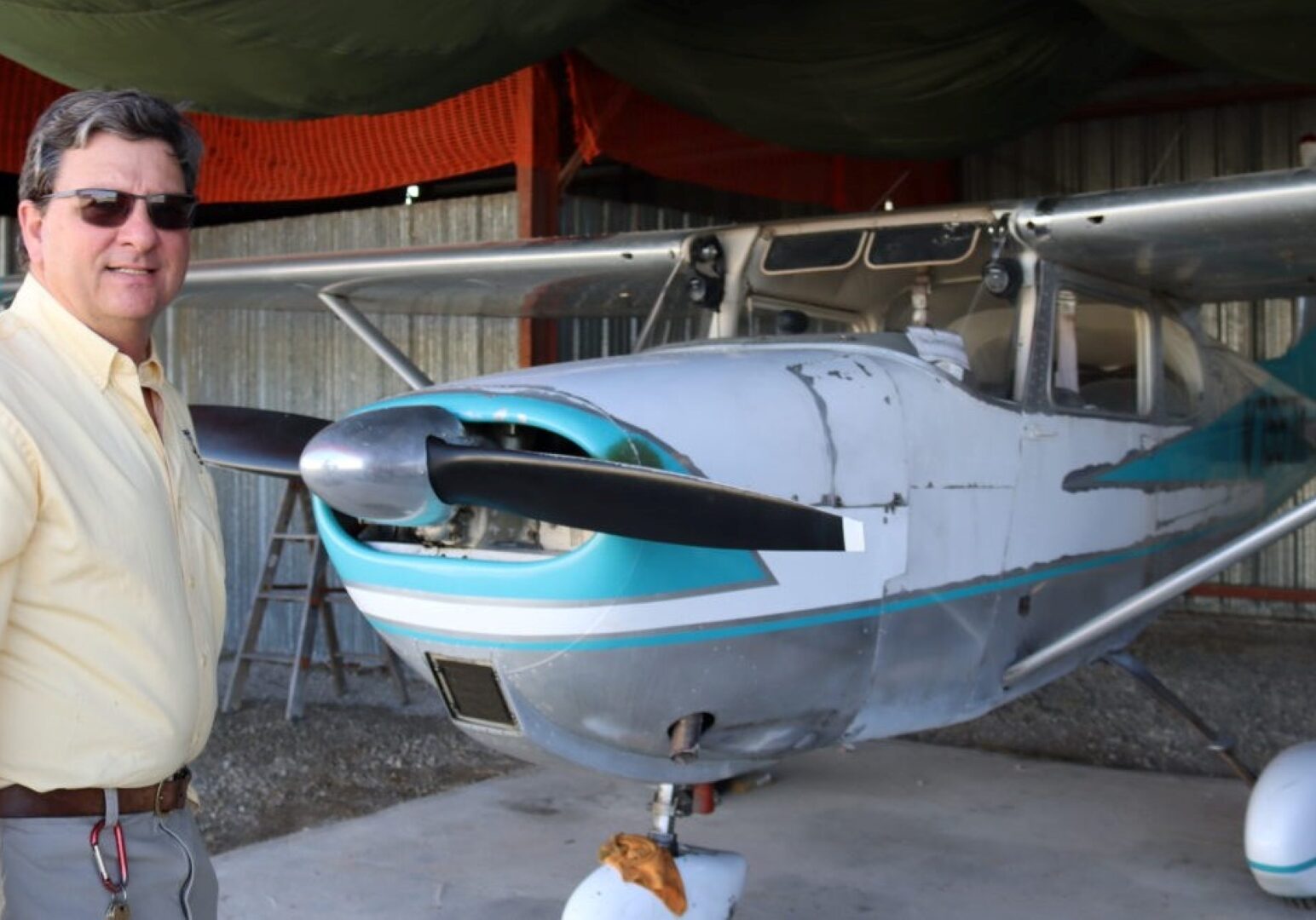 Man smiles in front of a small vintage propeller plane.