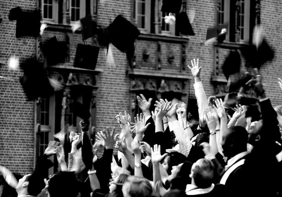 Black and white photo of group throwing graduation caps in the air.