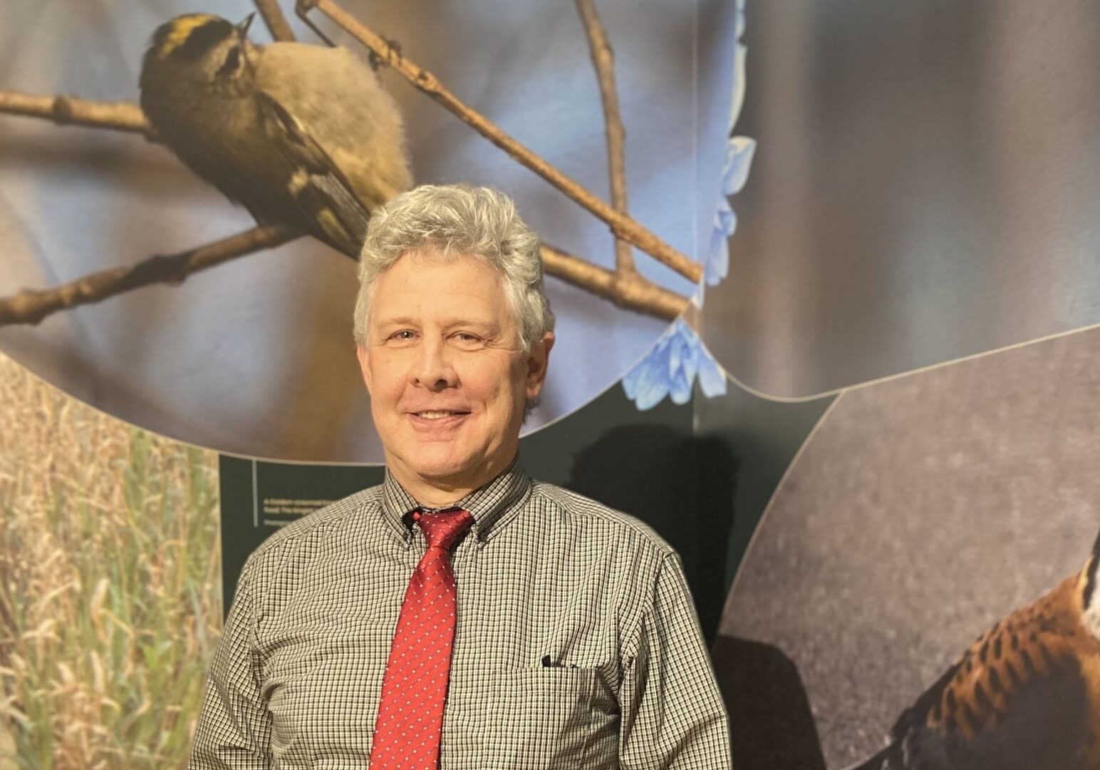 Eric Ward, vice president for public programming for Linda Hall Library, standing between two of his three photographs shown at the ornithology exhibition. Ward is particularly fond of the Brown-headed Nuthatch reintroduction display next to his pictures. He describes their distinct call as “sounding just like a rubber ducky.”