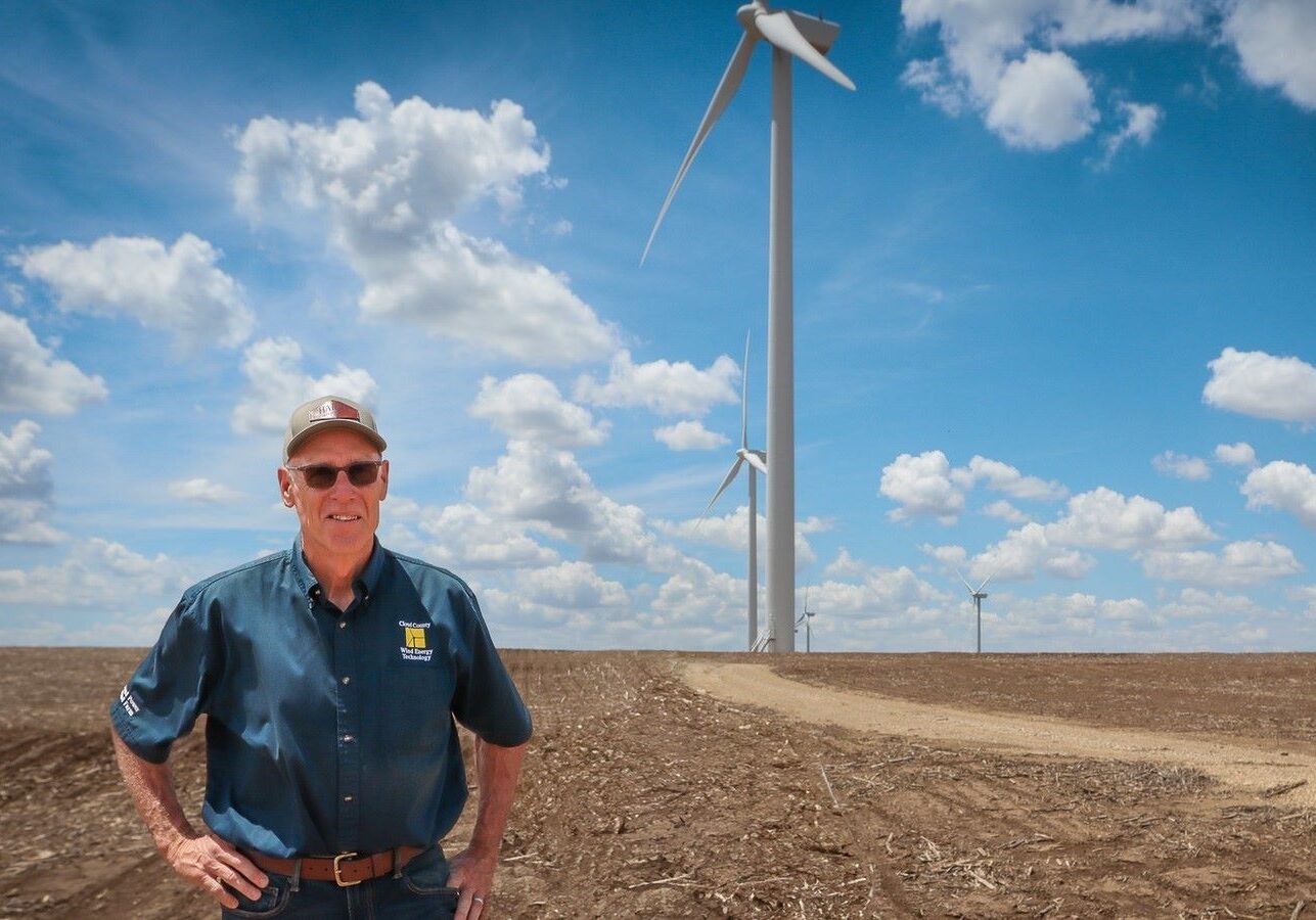 Bruce Graham, former head of the Renewable Energy Department at Cloud County Community College in Concordia, Kansas, stands in front of a wind turbine.