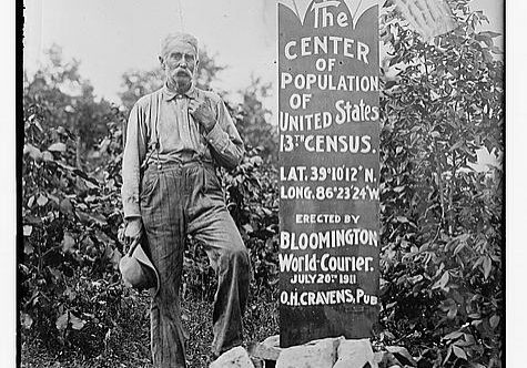 Man standing next to a sign that says "The Center of Population of the United States"