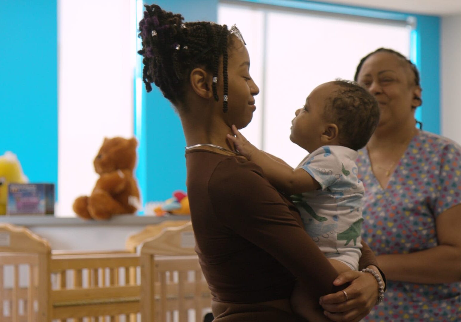 Woman holds young boy while older woman looks on in child care facility
