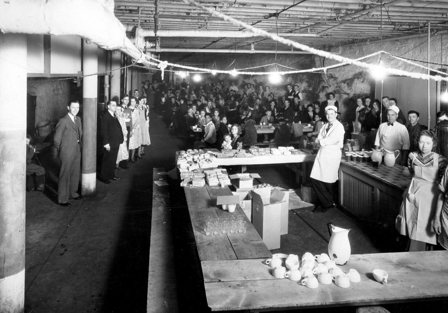 A photo from a 1930s mission Christmas season meal includes David Bulkley, in a dark suit at left and - holding a guest’s child at the nearby table - his daughter Ruth.