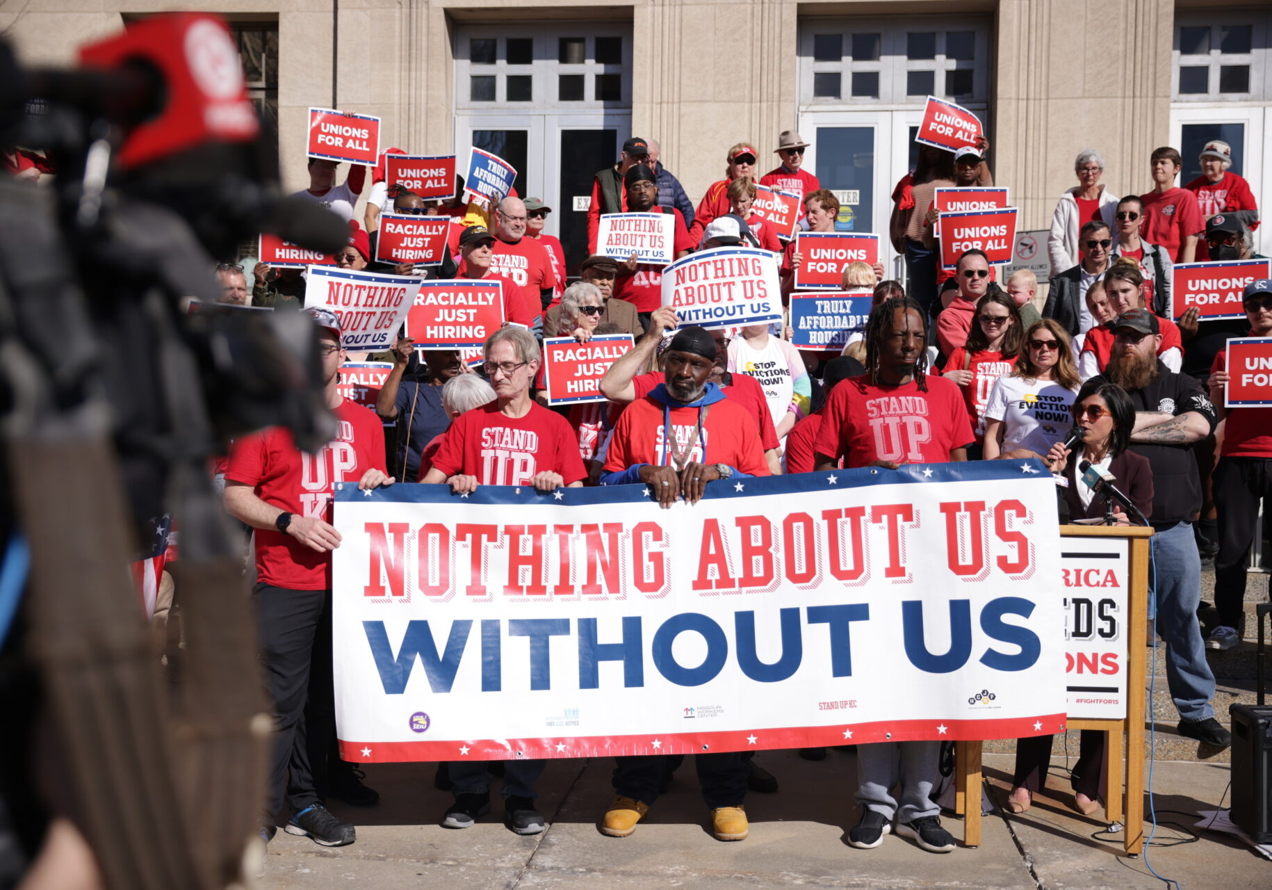 Group of activists in red T-shirts hold banner reading Nothing About Us Without Us