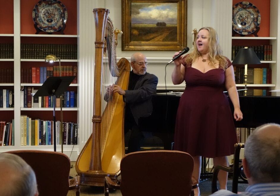 A woman singing next to a man playing a harp.