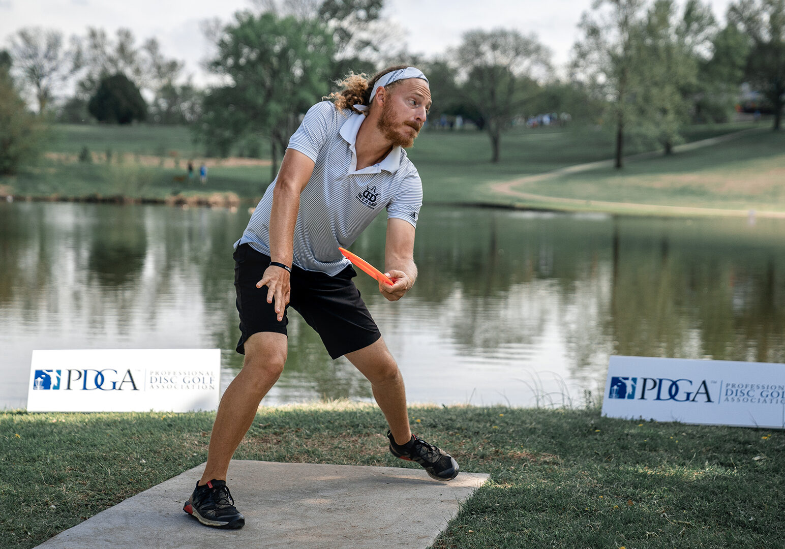 A disc golfer tees off from across a lake.