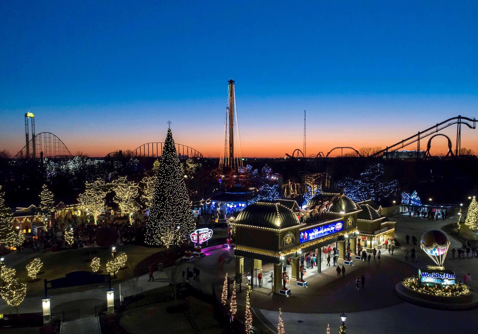 An aerial shot of Worlds of Fun lit up with Christmas lights at sunset.