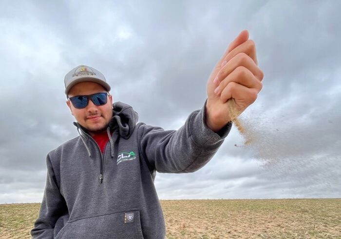 Farmer Alex Millershaski watches the wind blow a handful of dry, sandy soil across one of his wheat fields. His county in southwest Kansas just experienced its driest October on record.