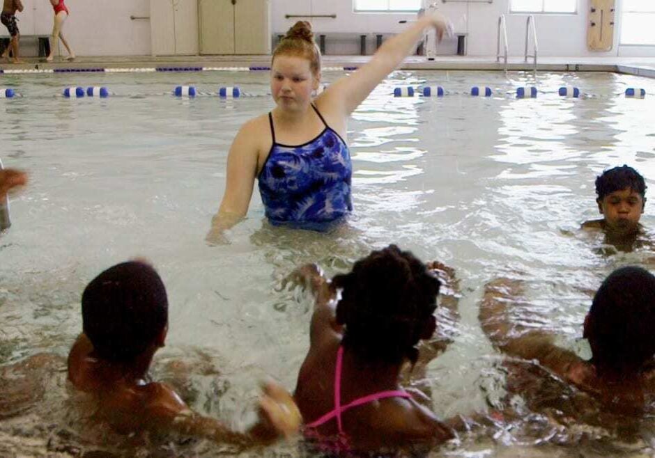 Woman teaching students to swim in pool.