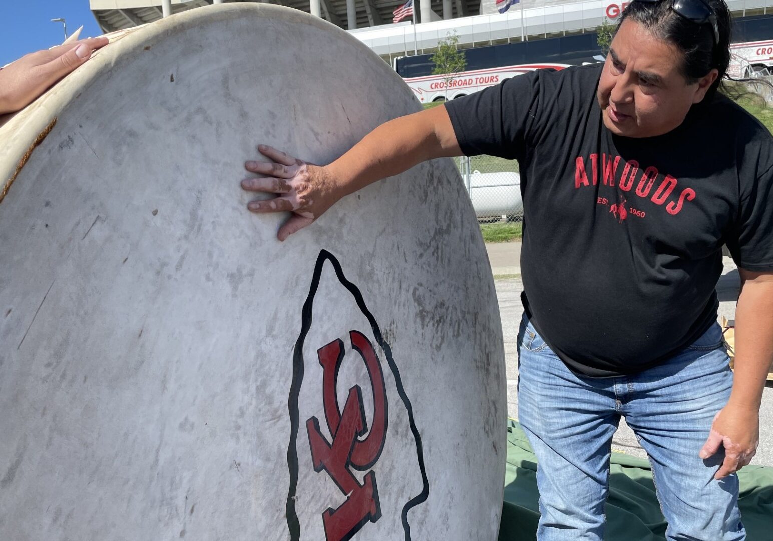 A man in a black t-shirt and jeans standing beside a large drum with a KC Chiefs logo.