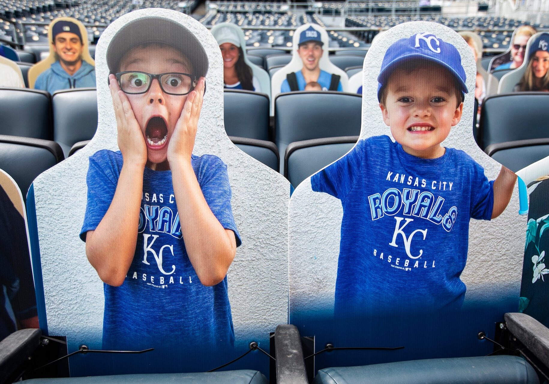 Two cardboard cutouts of fans resting in Kauffman Stadium's bleachers, ready for the home opener.