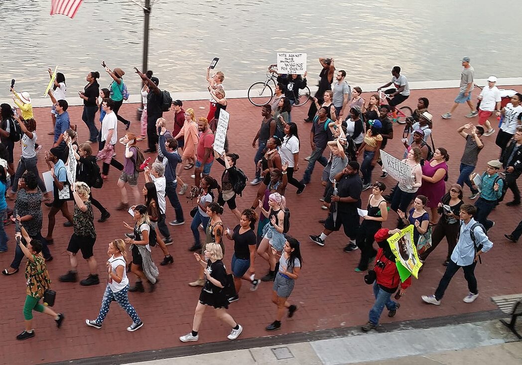 Photo of people marching in the streets, many with their hands up.