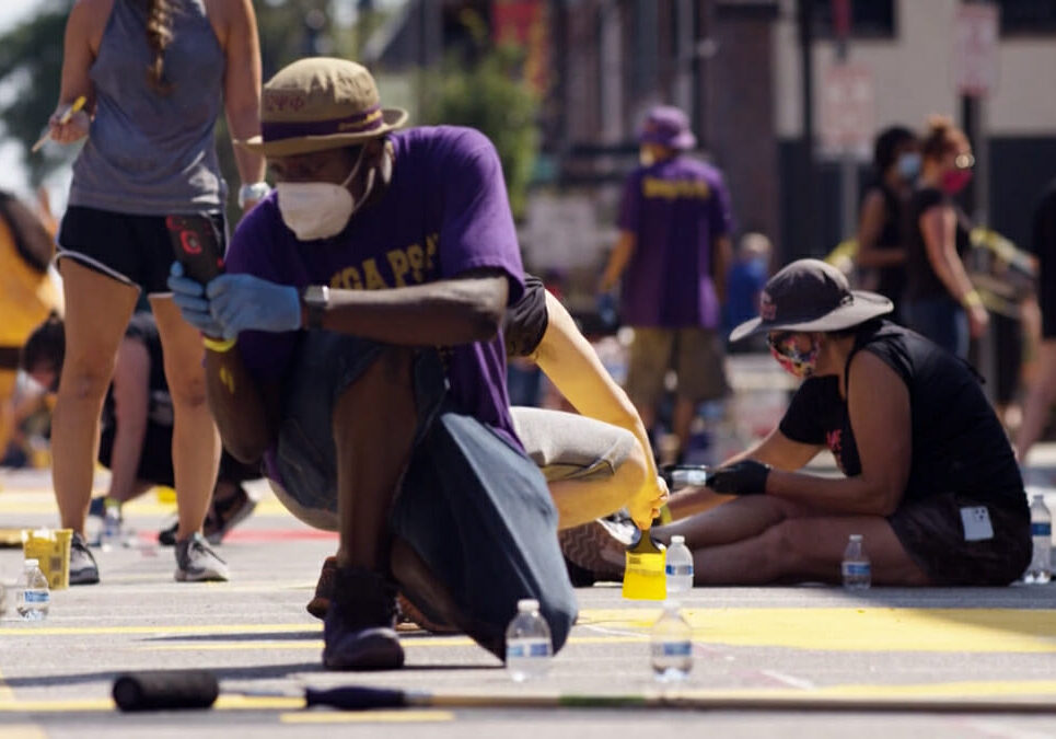 Man in hat and mask squats working on Black Lives Matter street in Kansas City.