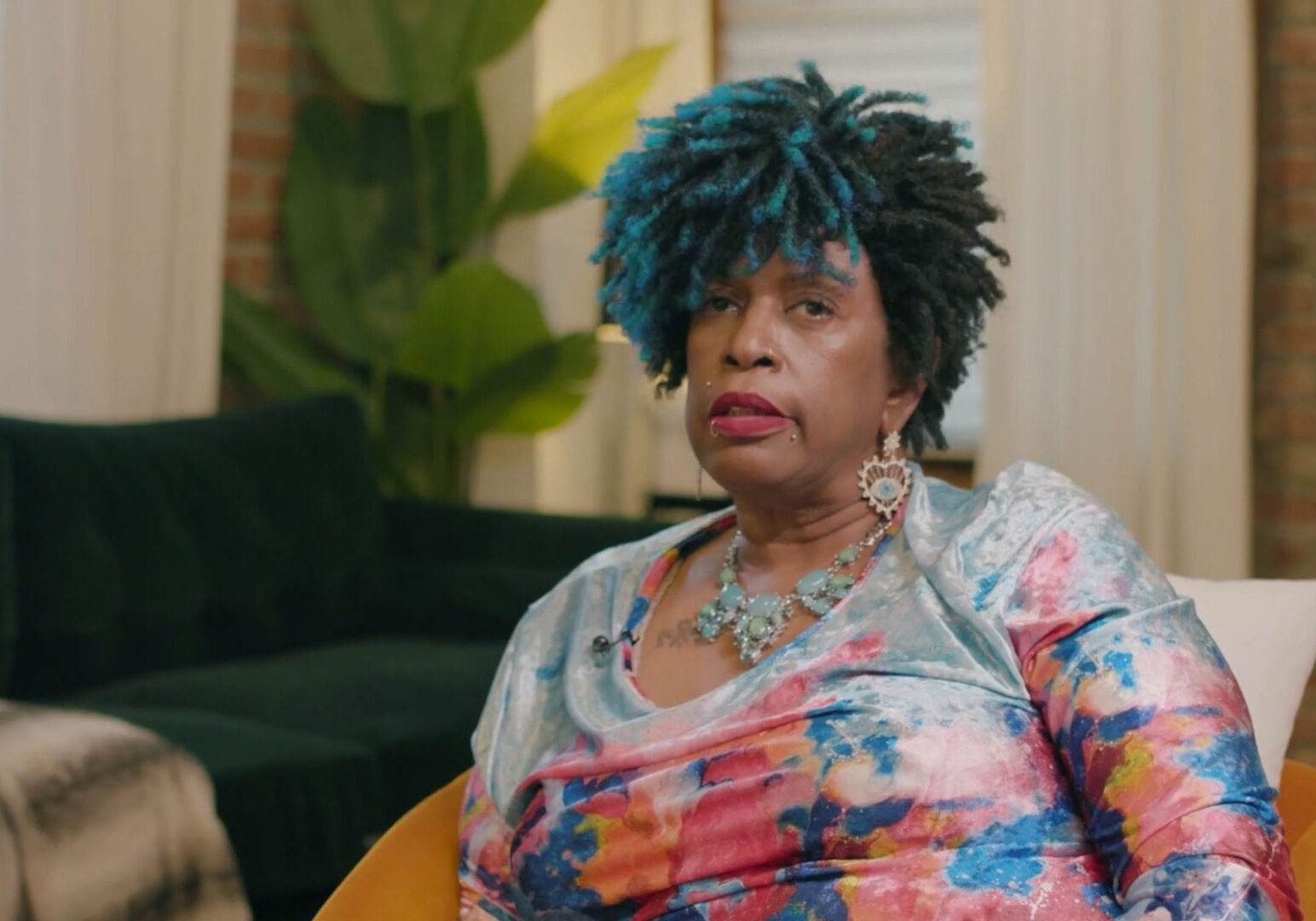 Woman with blue hair and colorful shirt sitting