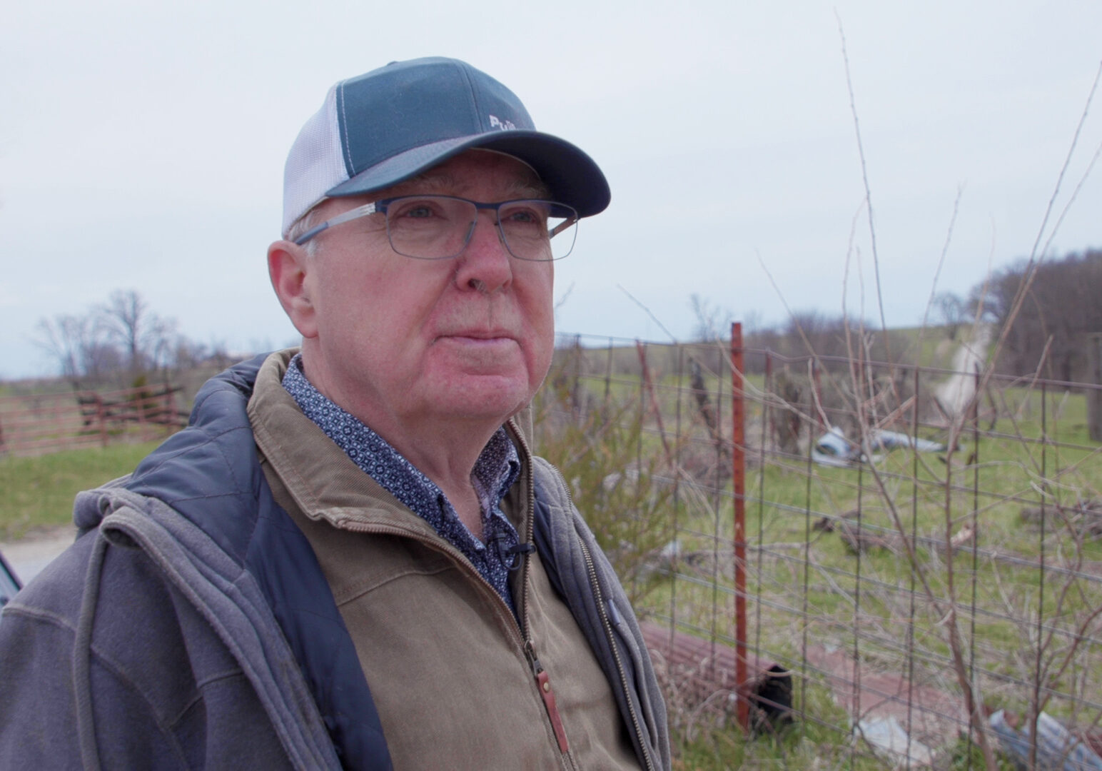 Man in a hat and glasses stands in front of rural l