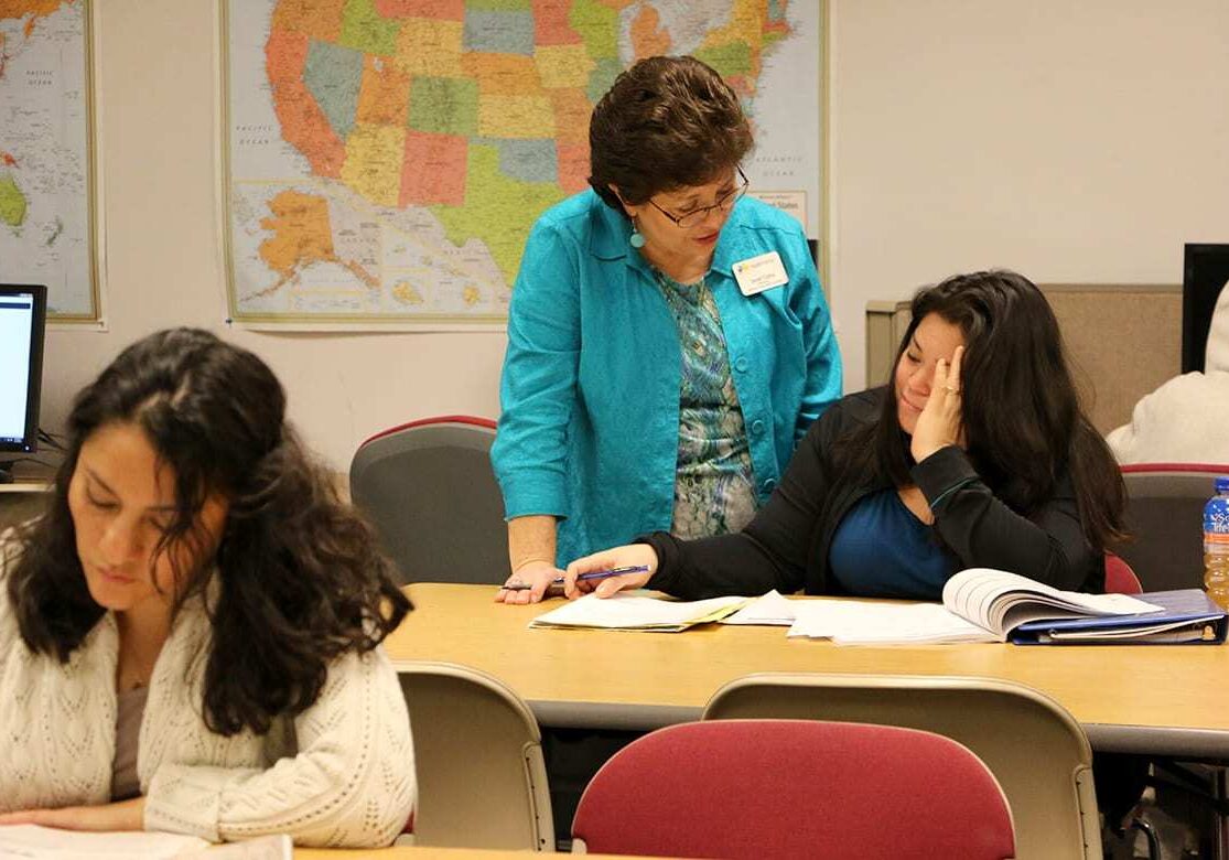 Image of woman standing next to woman seating at a desk.