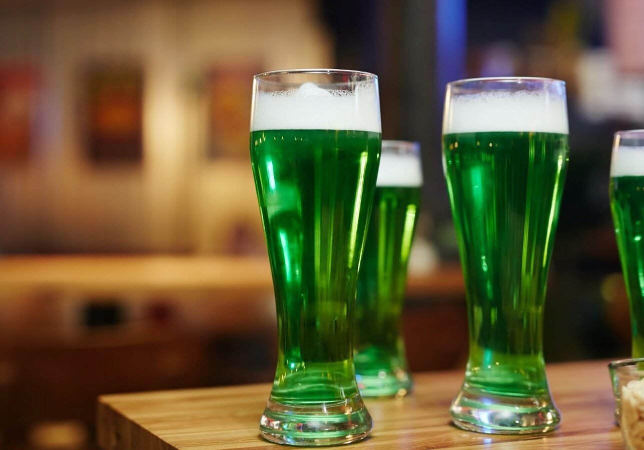 Four glasses of green beer on a bar.