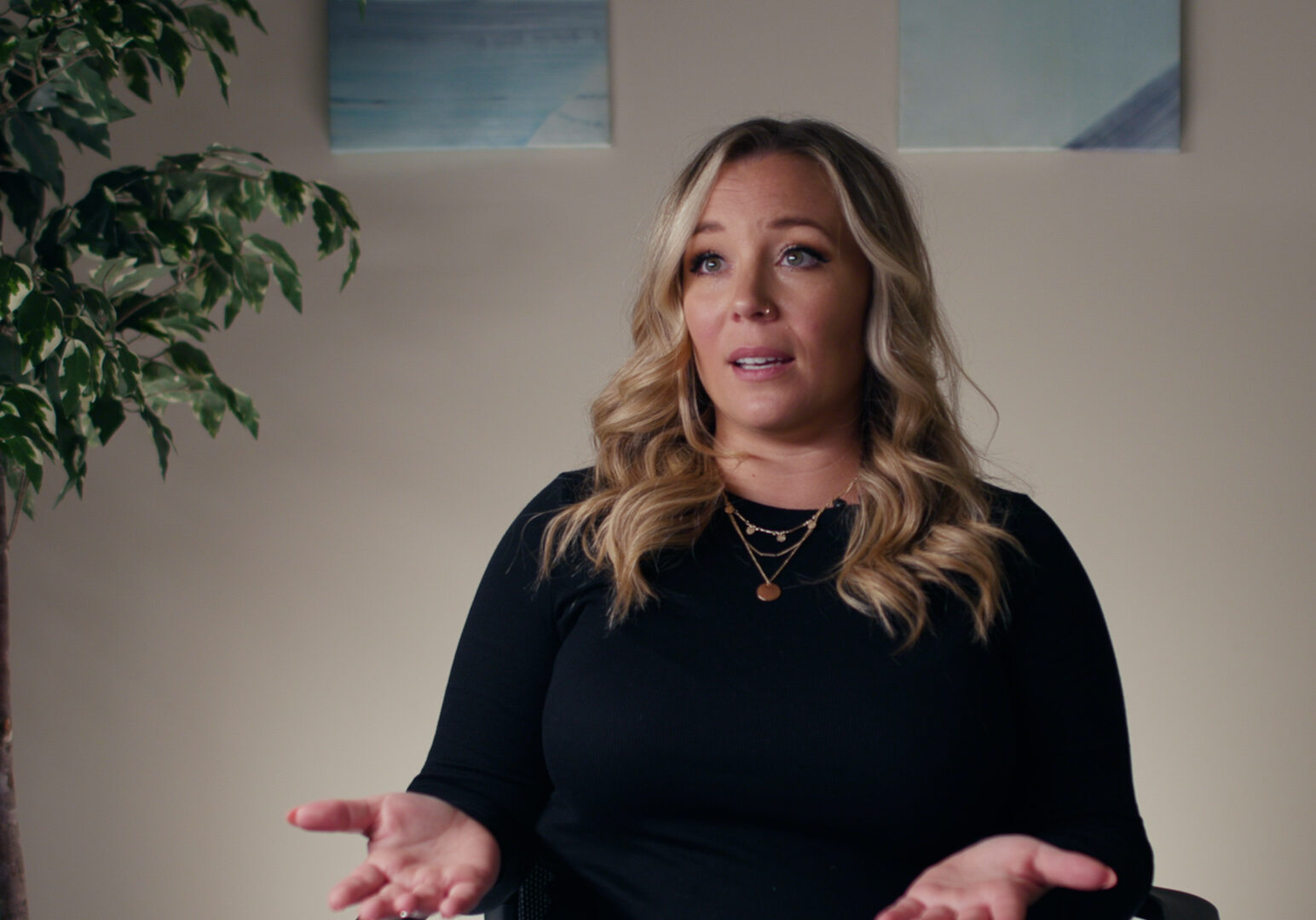woman with blonde hair and plant in the background.