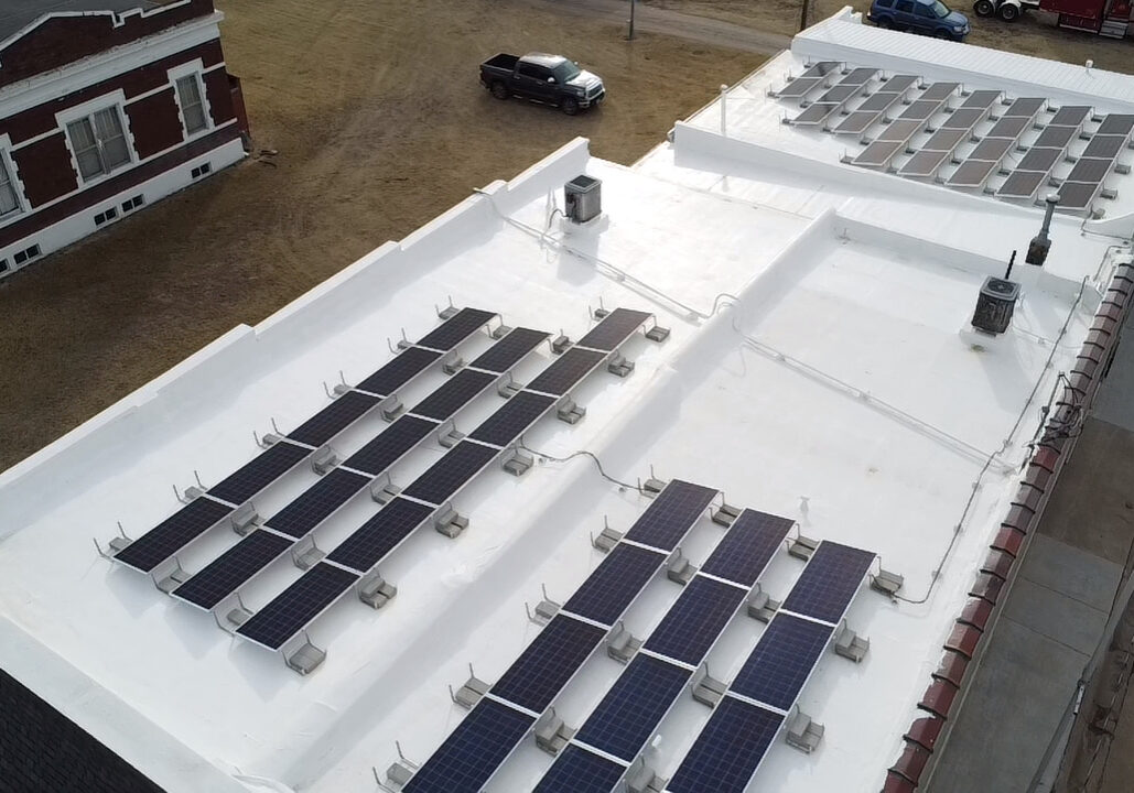 Rows of solar energy panels atop a white, flat roof of a small building.