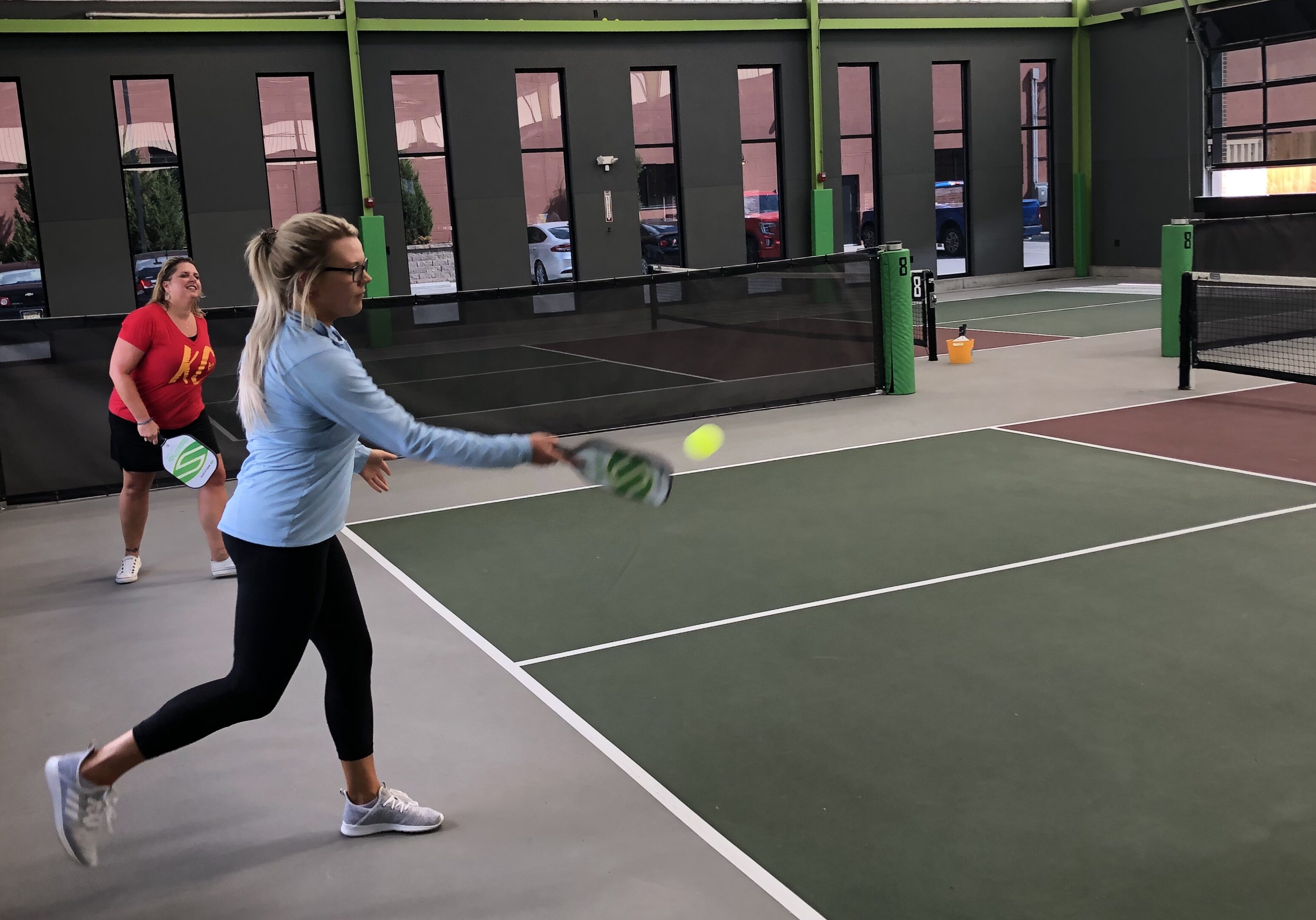 A woman serves the ball in a pickleball match.